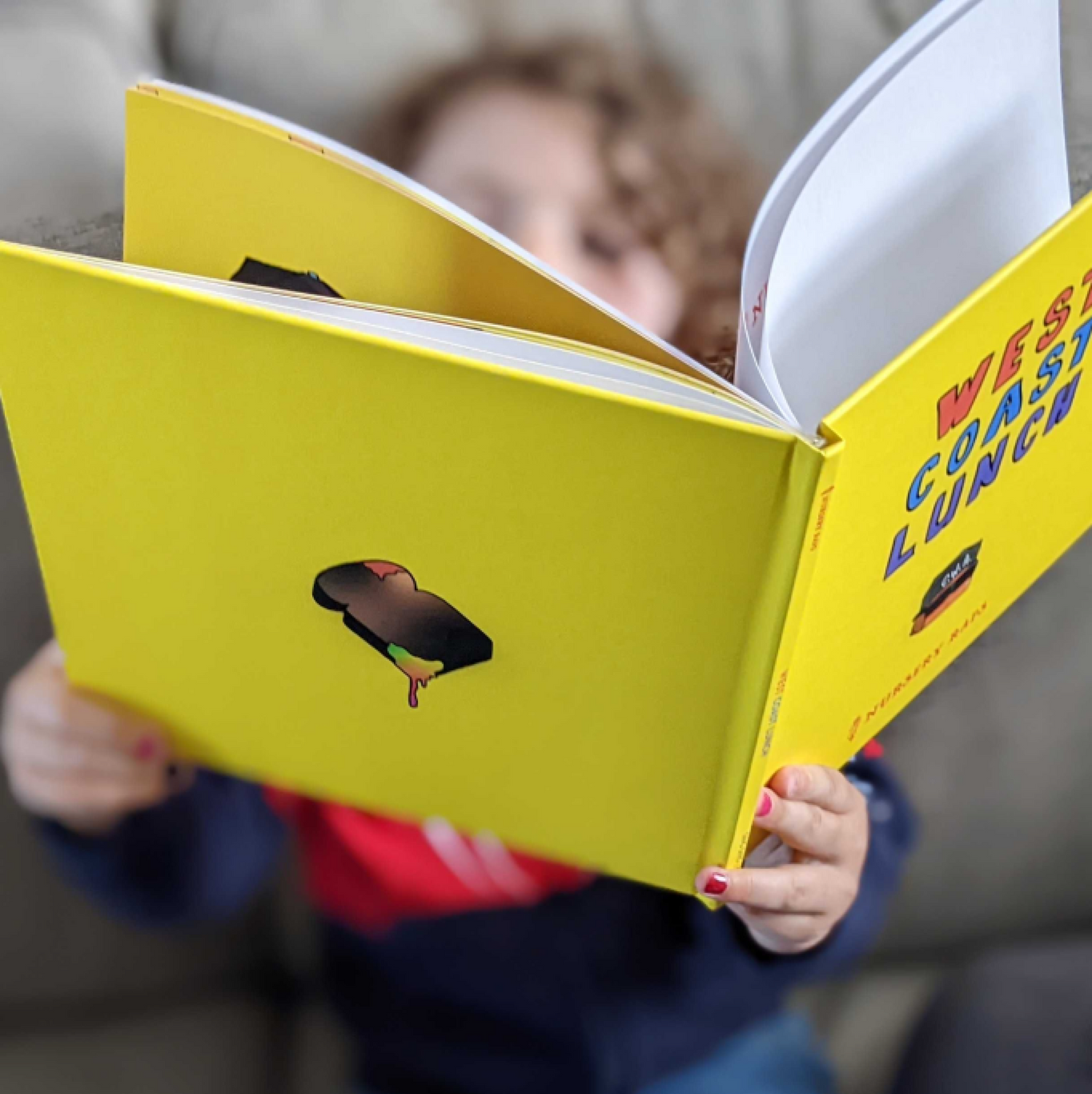 Child holding the kids book the West Coast Lunch book and reading or flipping through the pages.